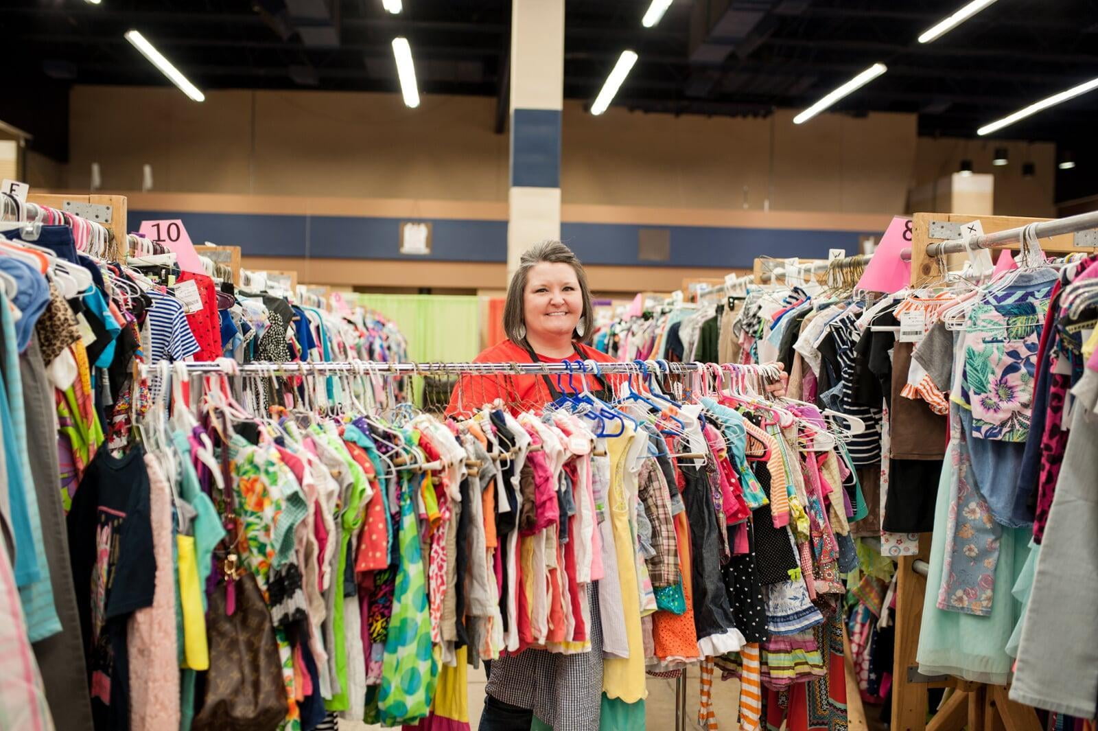 A smiling Team Member stands behind a rack of toddler girl&#039;s clothing at the sale.